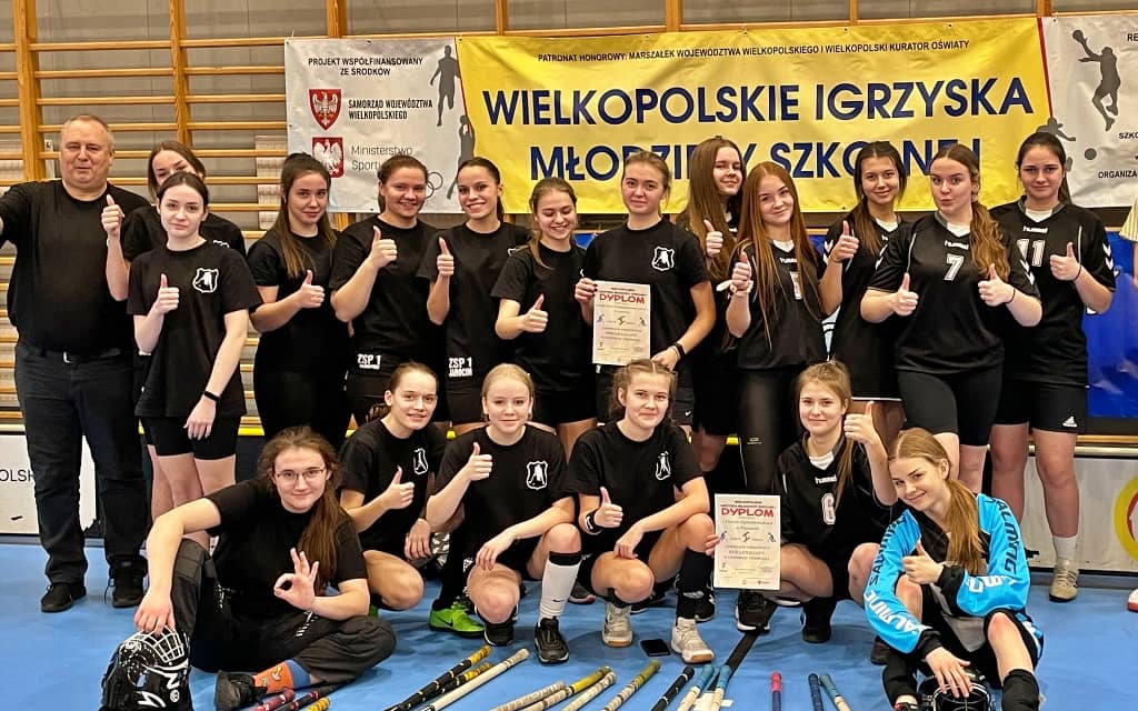 Na zdjęciu szkolna drużyna unihokeju dziewcząt. Zdjęcie zrobione w sali gimnazstycznej na tle baneru wielkopolskich igrzysk młodzieży szkolnej.