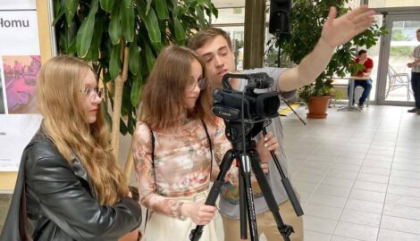 Na zdjęciu trzy osoby: instruktoró i dwie uczennice uczące się obsługiwać kamerę filmową.