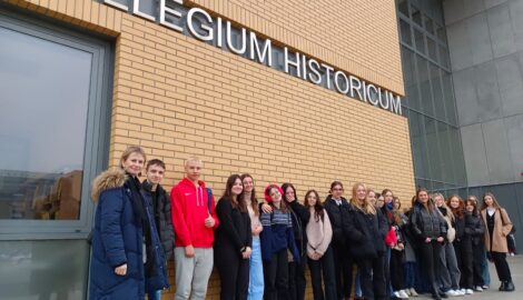 Na zdjęciu grupa uczniów wraz z nauczycielem pozują do zdjęcia przed budynkiem Collegium Novum w Poznaniu.