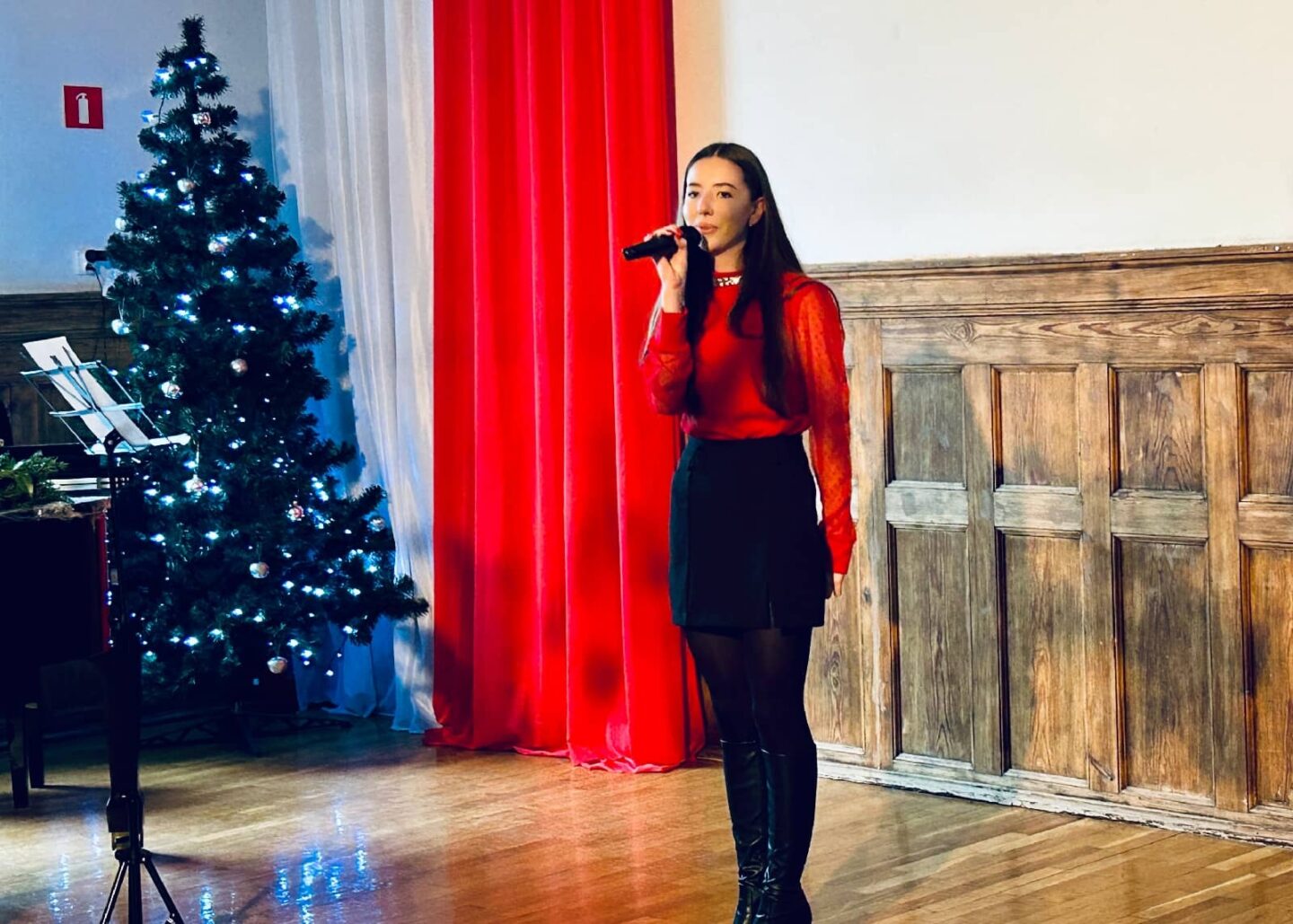 Za zdjęciu uczennica na scenie w szkolnej auli wykonuje utwór podczas świątecznego koncertu.