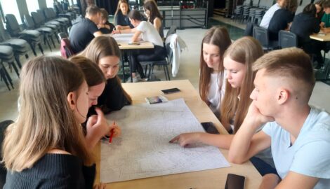 Na zdjęciu uczniowie podczas debaty dotyczącej przyszłości miasta Pleszew. Sześcioro uczniów siedzą przy stoliku i analizuje mapę miasta.