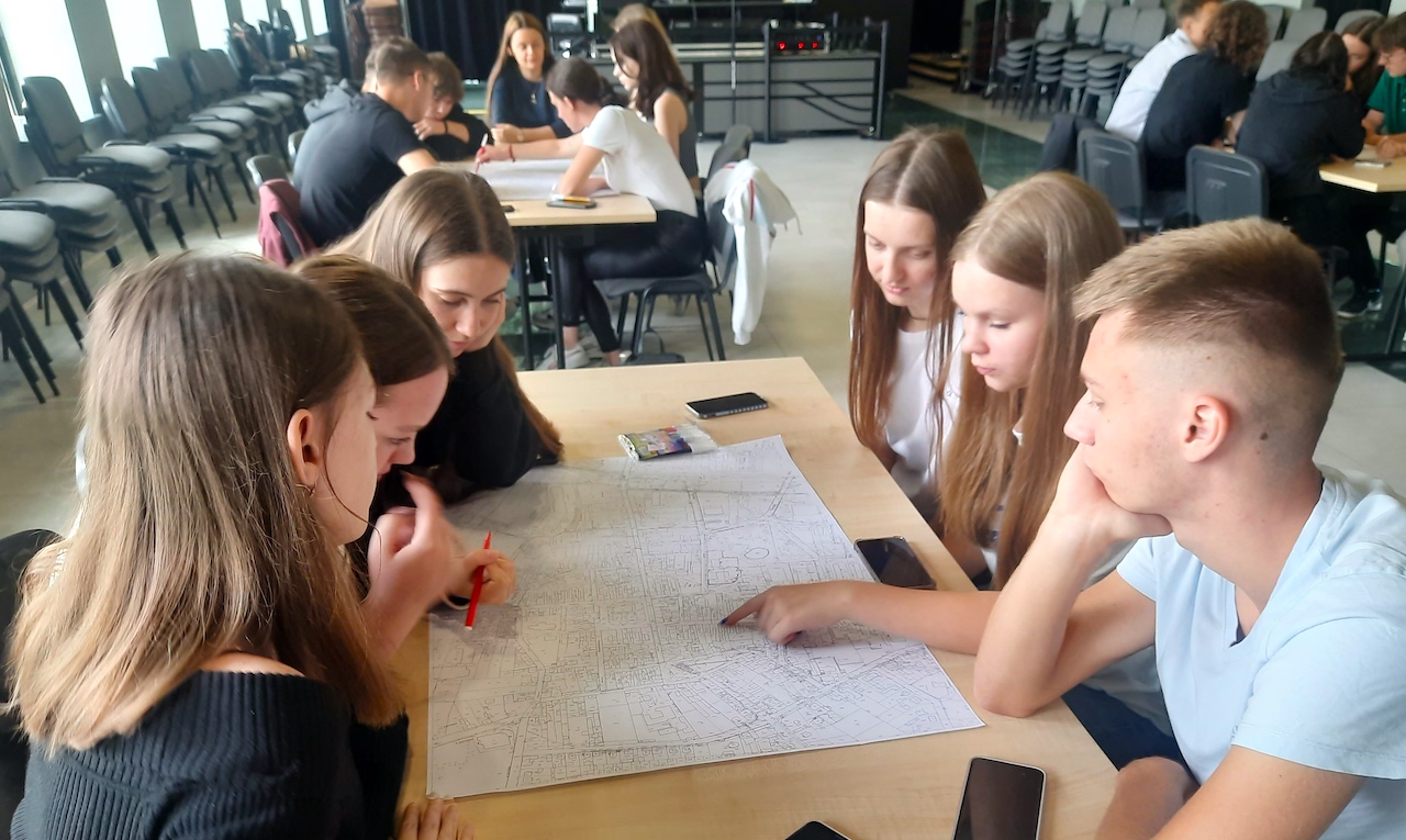 Na zdjęciu uczniowie podczas debaty dotyczącej przyszłości miasta Pleszew. Sześcioro uczniów siedzą przy stoliku i analizuje mapę miasta.