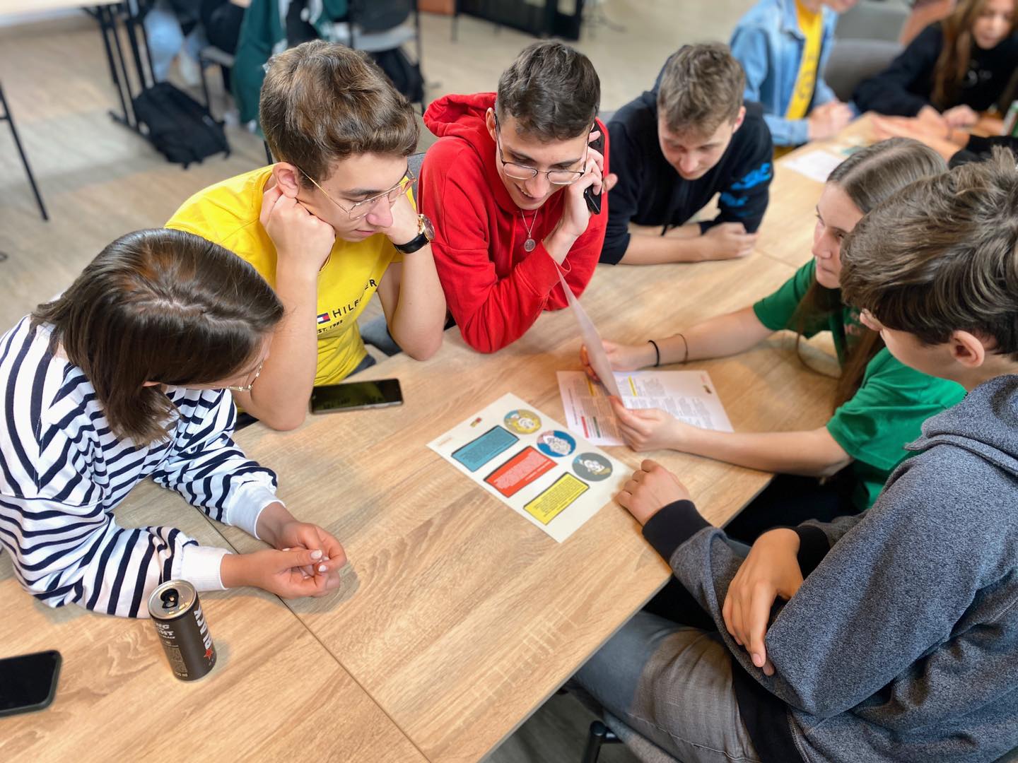 Na zdjęciu uczniowie podczas warsztatów pt. „Fakescape. Ucieknij fake newsom!” Uczniowie siedzą przy stole i rozwiązują projektowe zadania na kartach pracy.
