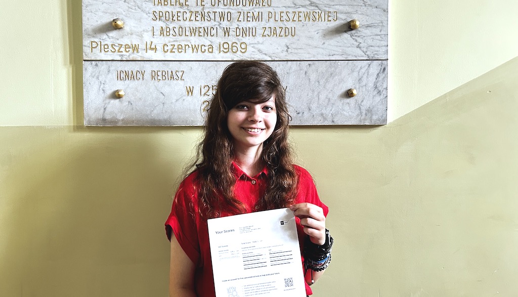Na zdjęciu uczennica na szkolnym korytarzu prezentuje dyplom.