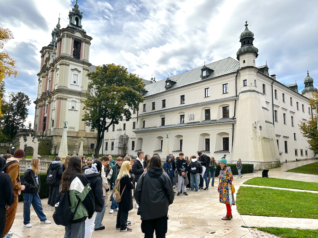 Grupa uczniów podczas krajoznawczej wycieczki w Krakowie. Na pierwszym planie przewodnik, a w tle historyczny kościół.