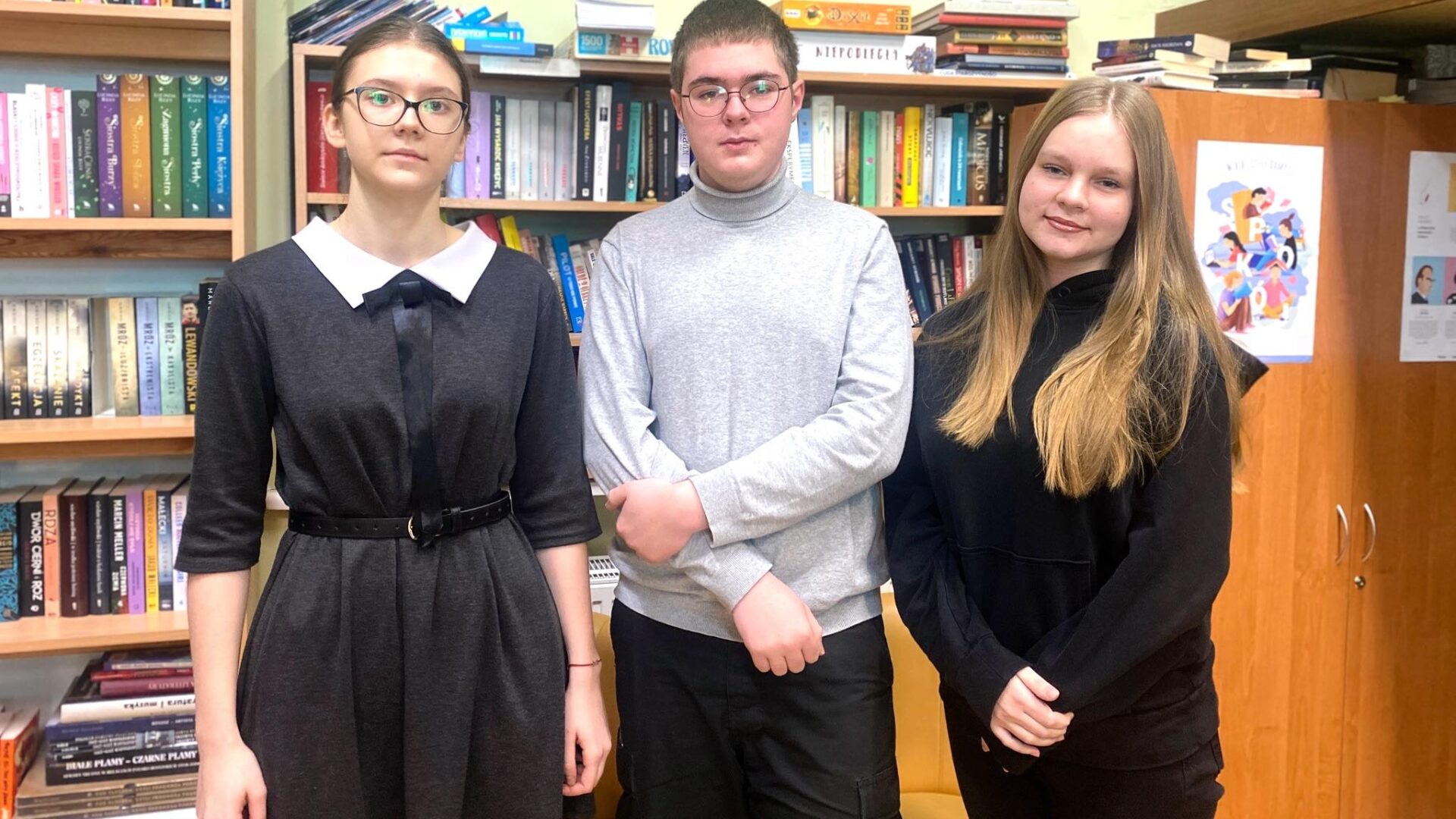 Na zdjęciu trójka uczniów, którzy zakwalifikowali się do finału konkursu biologicznego. Uczniowie stoją w szkolnej bibliotece na tle półek z książkami.