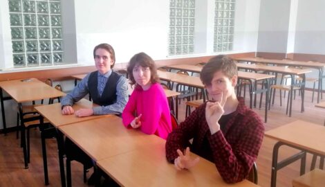 Na zdjęciu trójka uczniów uczestniczących w rywalizacji Liga Przedmiotowa z języka angielskiego. Trójka uczniów siedzi w ławce przed ekranem, na którym odbywa się rywalizacja.