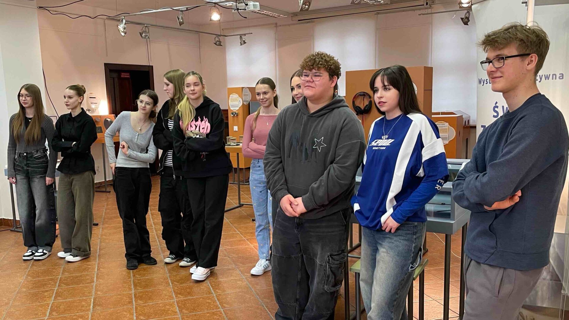 Na zdjęciu uczniowie w regionalnym muzeum. Przed grupa uczniów opiekun wystawy, który wyjaśnia uczniom istotę wystawy.