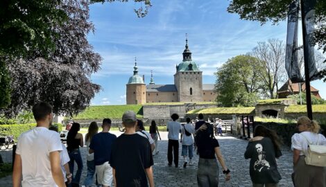 Zdjęcie uczniów z wycieczki do Szwecji. Na pierwszym planie grupa uczniów idąca zwiedać średniowieczny zamek. W tle widać baszty zamkowe.