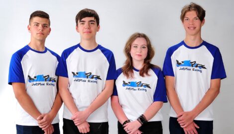 Na zdjęciu grupa czterech uczniów na biały tle. Uczniowie ubrani są w koszulki z napisem JetPlex Racing - stanowiący nazwę drużyny uczestniczącej w konkursie.