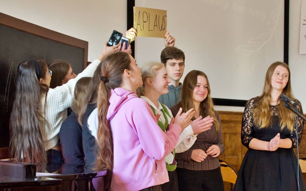Na zdjęciu uczniowie na scenie w szkolnej auli podczas występu z okazji dnia nauczyciela.