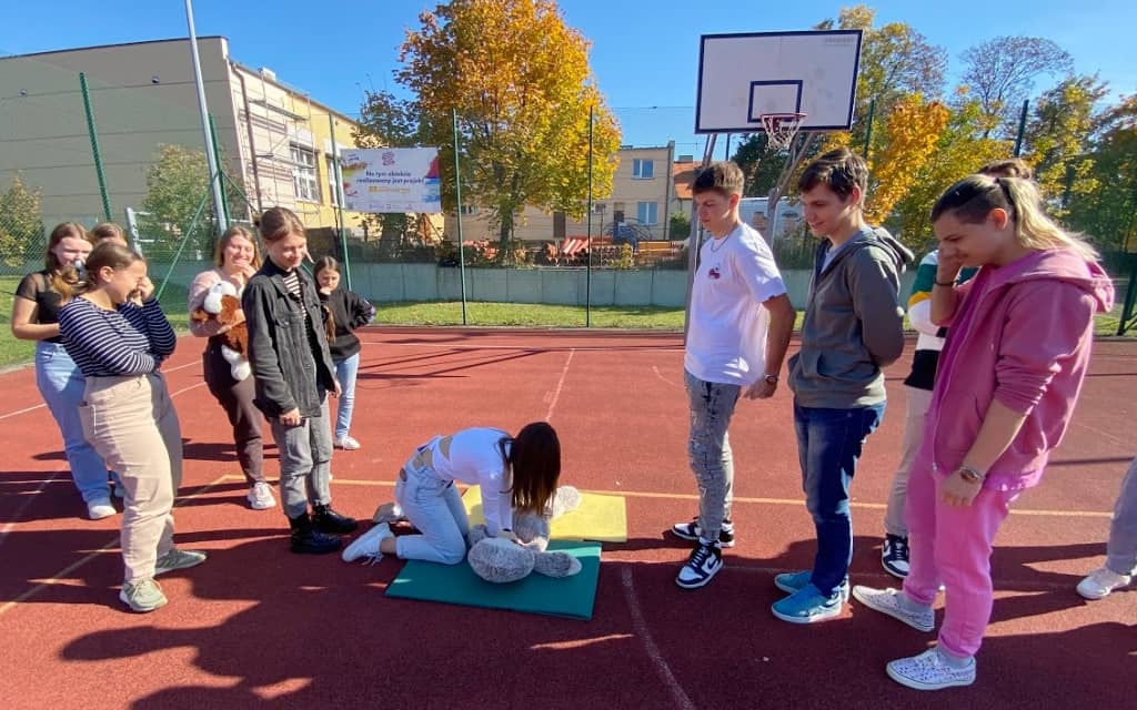 Na zdjęciu uczniowie na szkolnym boisku podczas treningu prowadzania resuscytacji krążeniowej.