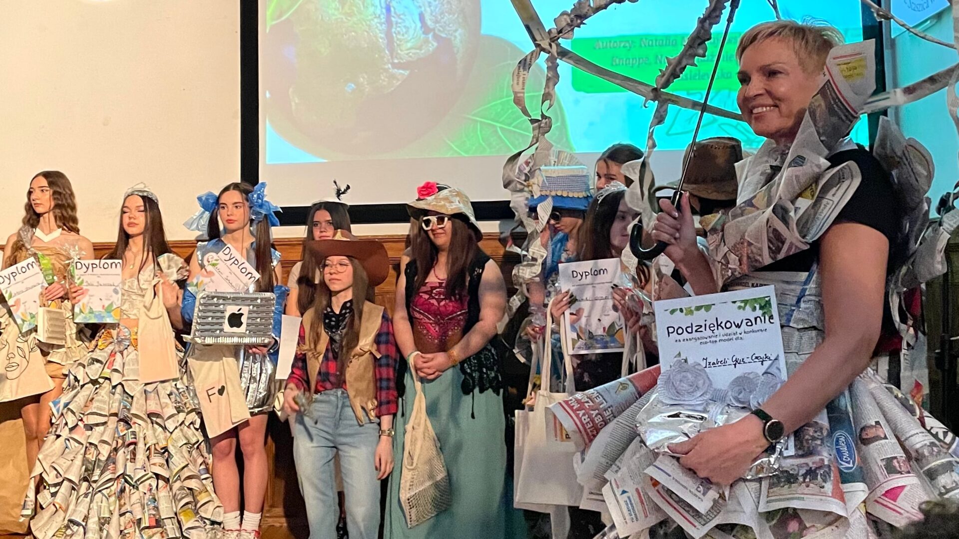 Na zdjęciu uczestnicy pokazu mody - Eco Top Model. Uczestnicy odbierają dyplomy na scenie.