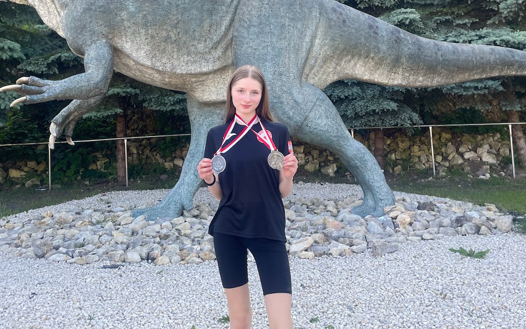 Na zdjęciu uczennica stoi w parku i prezentuje dwa medale zdobyte w zawodach w kickboxingu.